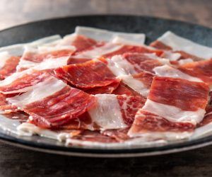 Spanish serrano ham slices on black plate on wooden table